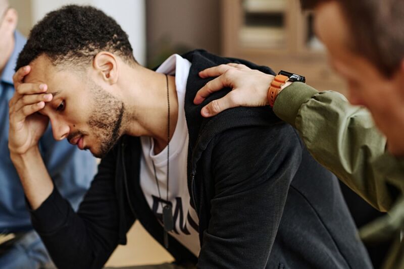 A concerned man with his head in his hand is being comforted by another person, showing potential signs of cocaine addiction.