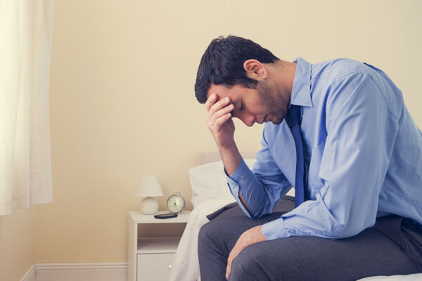 A depressed man sitting head in hands on his bed, illustrating the profound impact of sleep deprivation on mental health