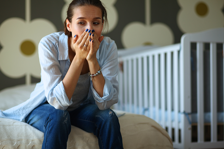 A distressed woman sitting on a bed in a child's room, highlighting the need for EMDR therapy for childhood trauma in adults