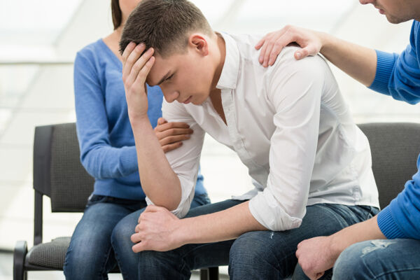 A group of people supporting a distressed young man, highlighting the importance of addiction intervention for alcohol rehab