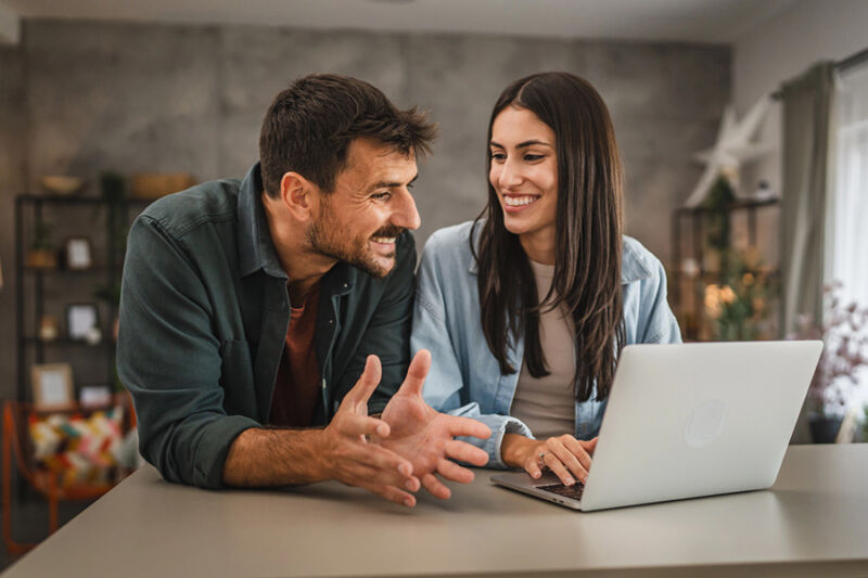 A smiling couple discusses intensive outpatient treatment options while using a laptop at home, suggesting research or planning.