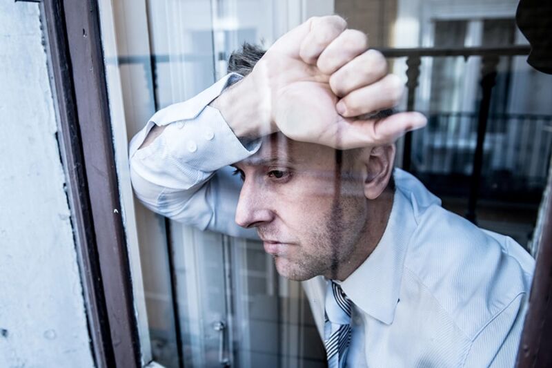 A stressed man leans on a window, showing signs of anxiety and depression, which can be linked to drug dependency.