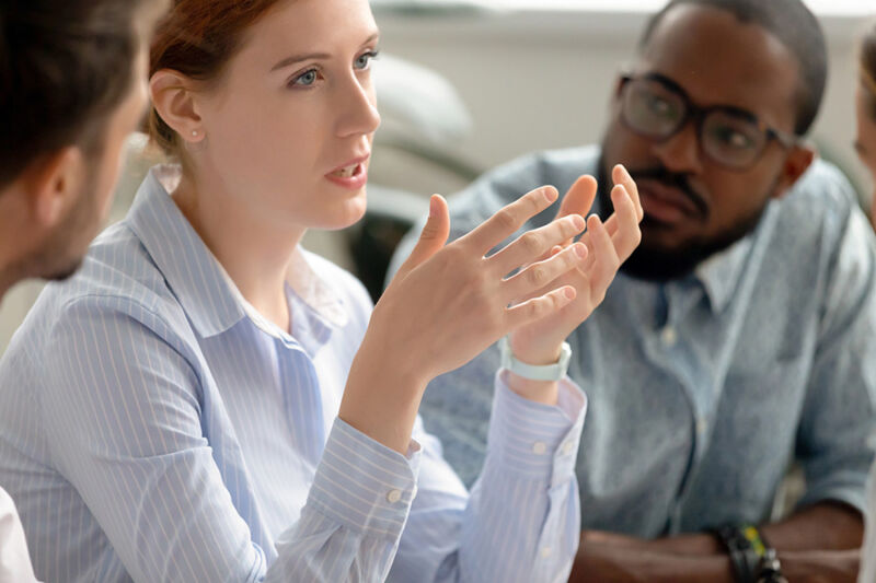 A woman gestures while speaking during a group discussion in a partial hospitalization therapy session, with two others listening