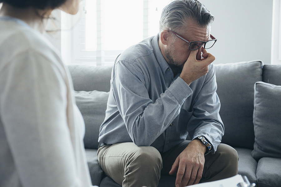 Distressed man in therapy session at a personality disorder treatment center, seated on a couch with a therapist in view