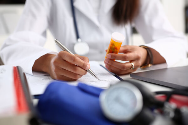 Doctor holding a prescription bottle and writing notes, representing medication-assisted treatment and in-network TRICARE rehab coverage.