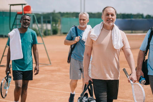 Group of men with tennis gear smiling on a court at our Arizona luxury rehab, showcasing wellness and recreational activities.