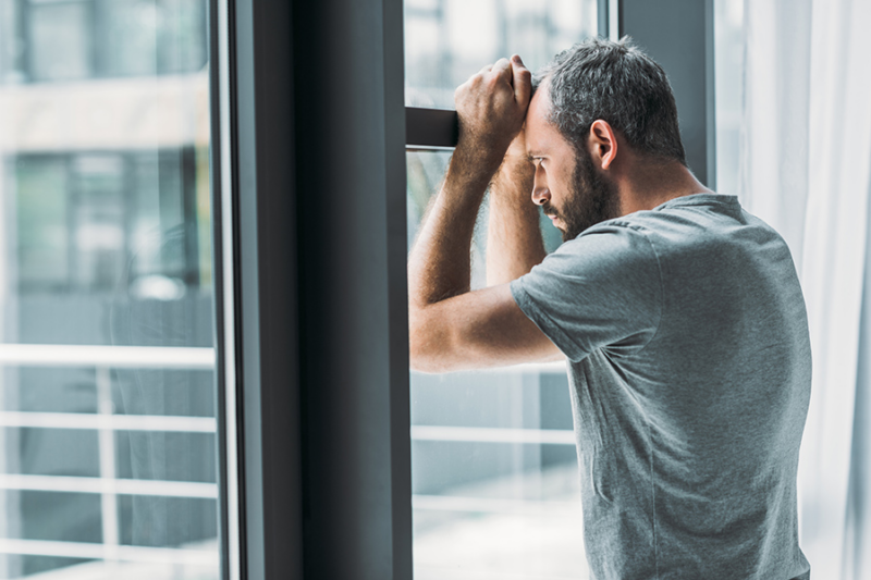 Man leaning on a window, looking distressed, symbolizing suffering from dual diagnosis