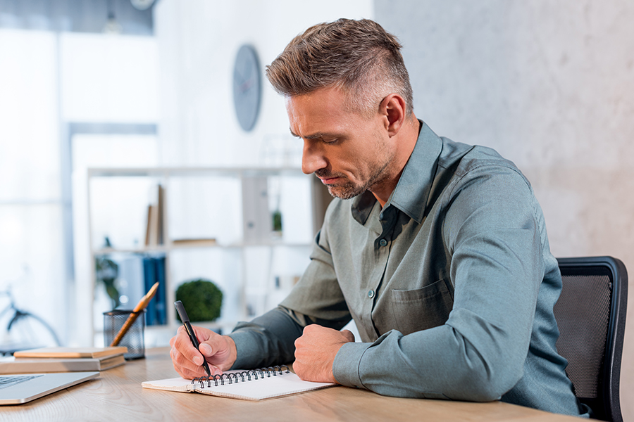 Man, writing in a notebook at a desk, focused on how to plan an intervention effectively.