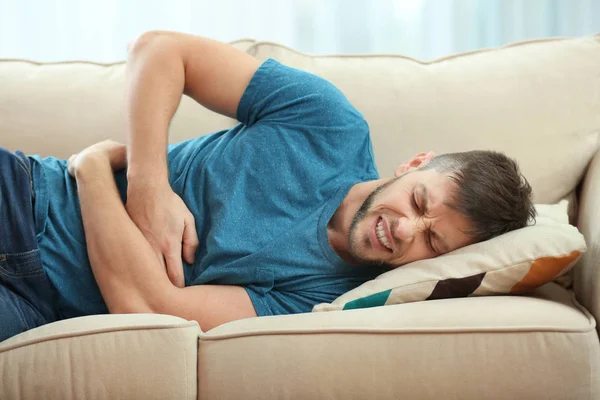 Young man experiencing stomach ache, a common physical symptom of alcohol abuse