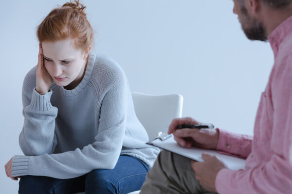 Young woman in DBT therapy session appears distressed, holding her head